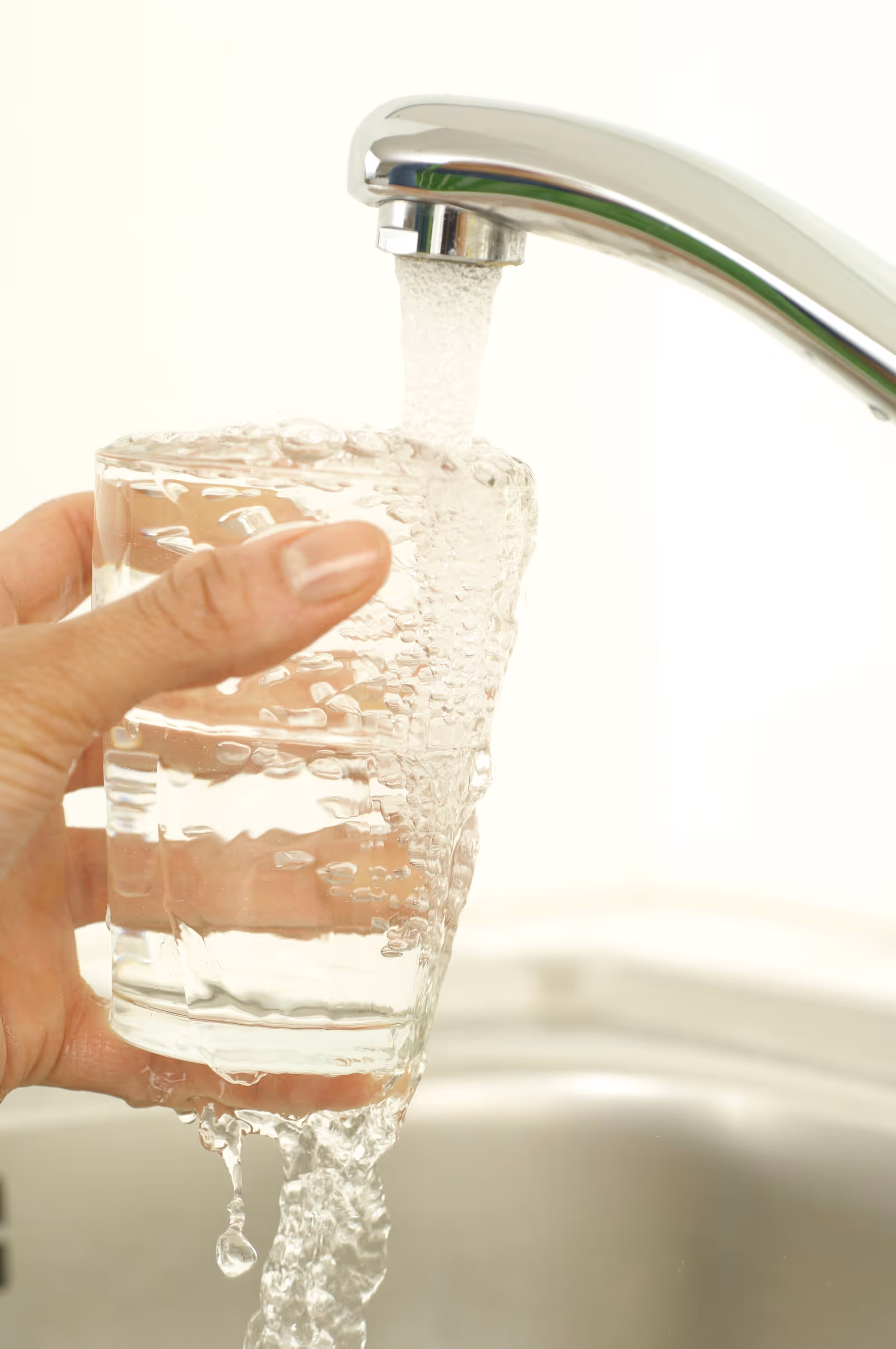 A kitchen tap running into a clear glass; bacteria in well water has no color, taste, or smell, so safe-looking water can still be contaminated