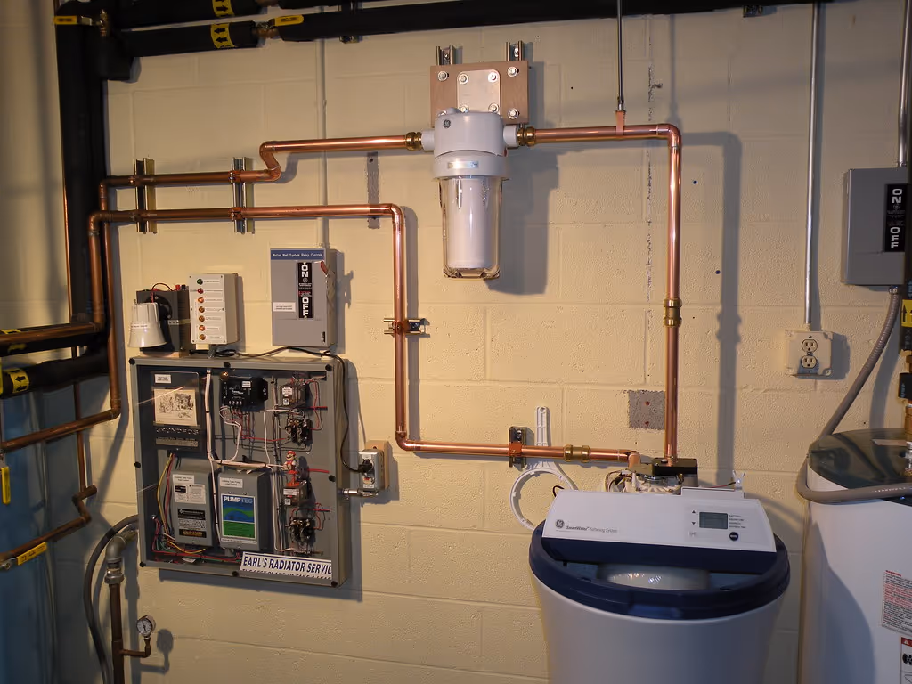 A whole-house water filter and softener installed on the main water line in a basement, with copper piping and control panels