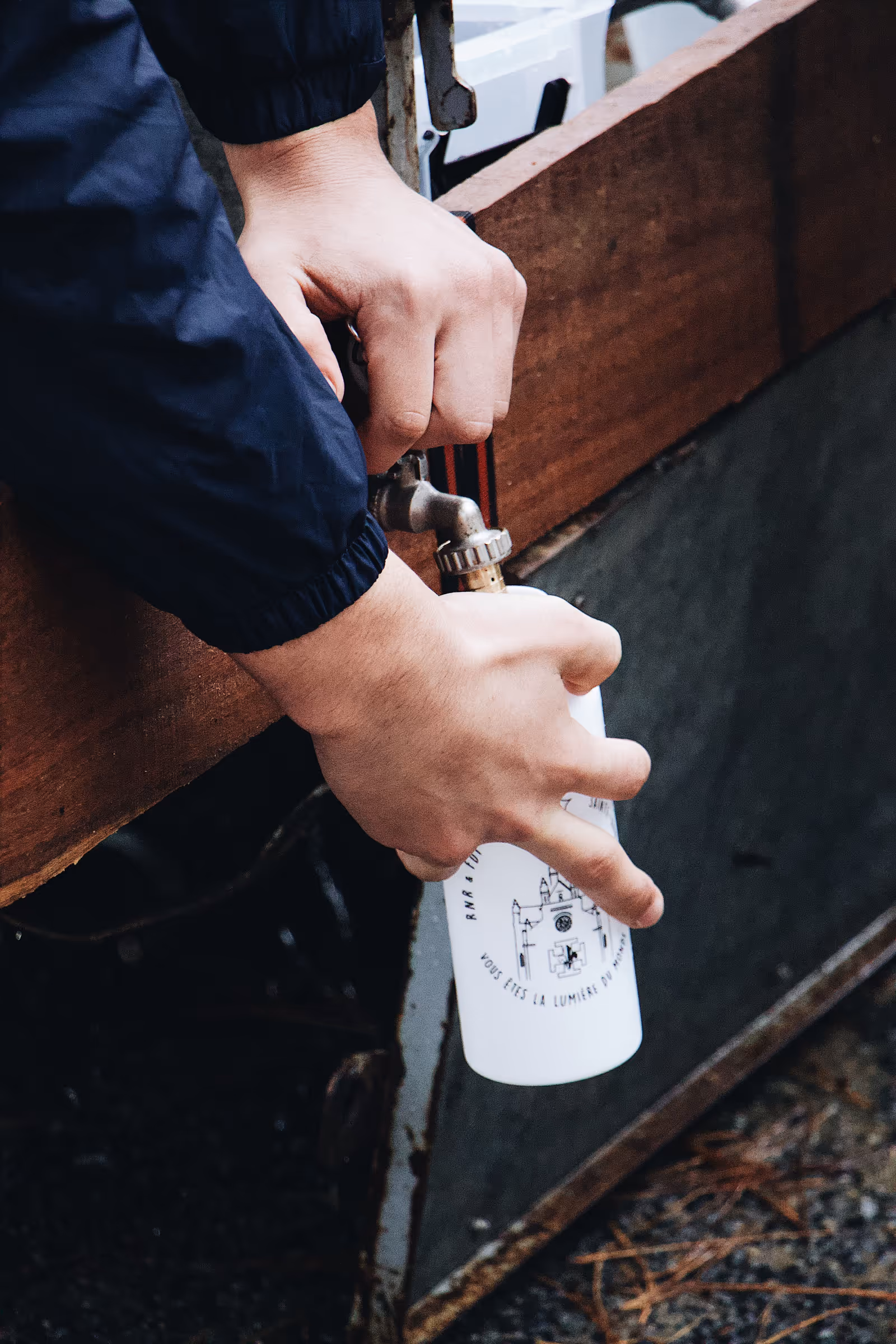 Hands filling a bottle with water from an outdoor tap, the same motion as drawing a sample for a lab test kit