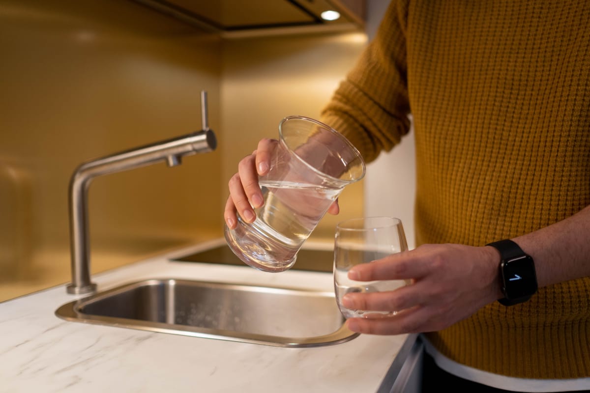 A person pouring water into a clear drinking glass in a bright modern kitchen